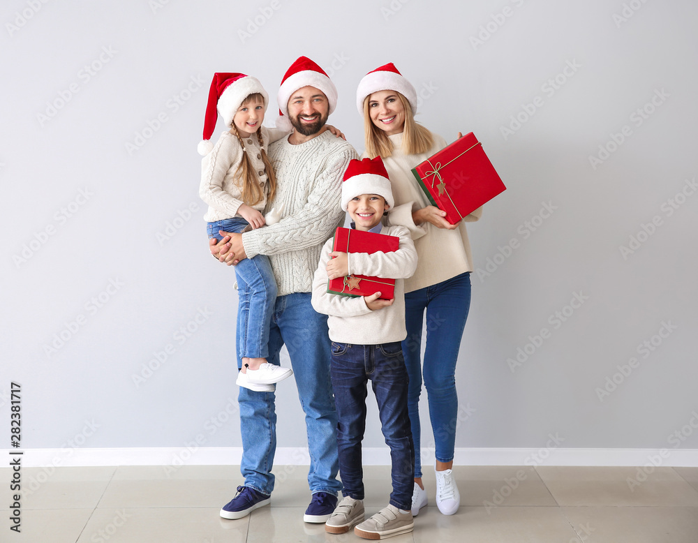 Happy family with Christmas gifts near light wall