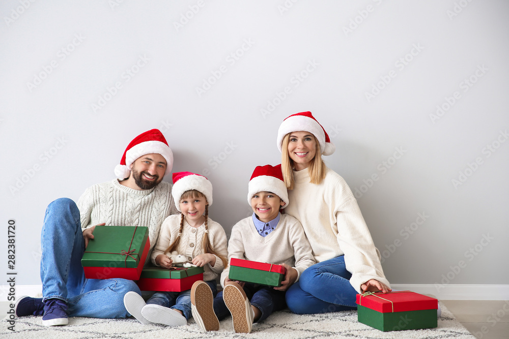 Happy family with Christmas gifts sitting near light wall