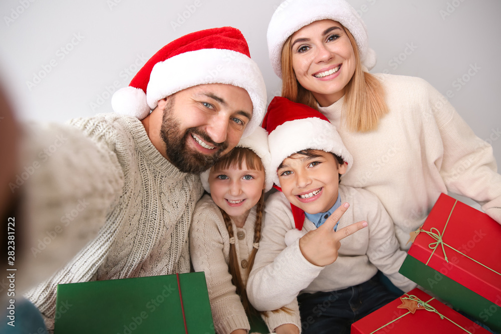 Happy family with Christmas gifts taking selfie on light background