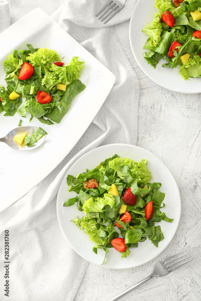 Plates with fresh tasty salad on light table