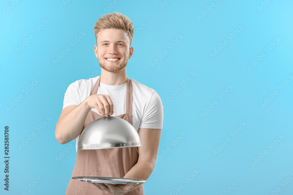 Handsome male chef with tray and cloche on color background