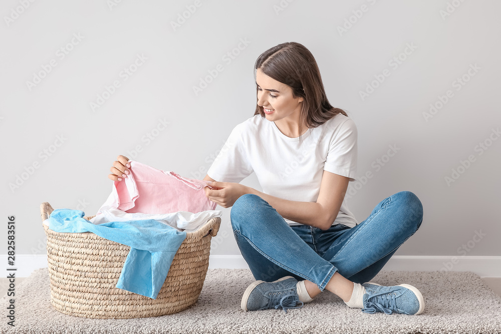 漂亮的年轻女子坐在靠近白墙的地板上洗衣服