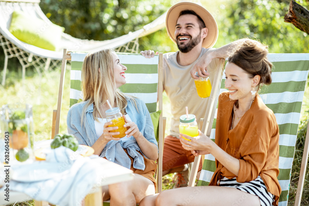 Young friends talking and having fun, while sitting together with summer drinks on the sunbeds at th