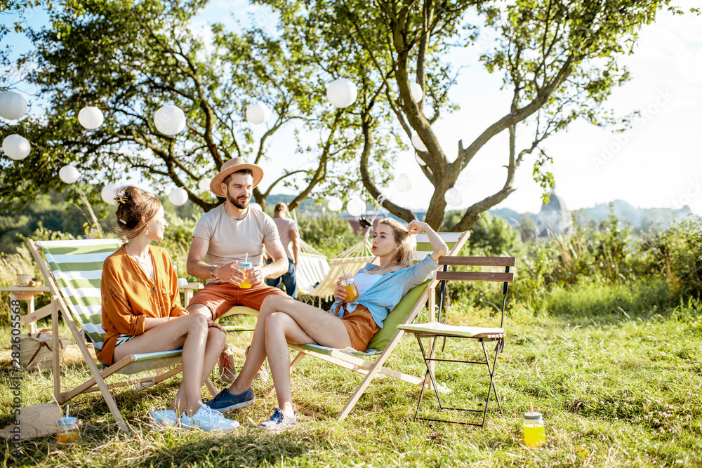 Young and cheerful friends relaxing with drinks, sitting on the sunbeds in the beautifully decorated