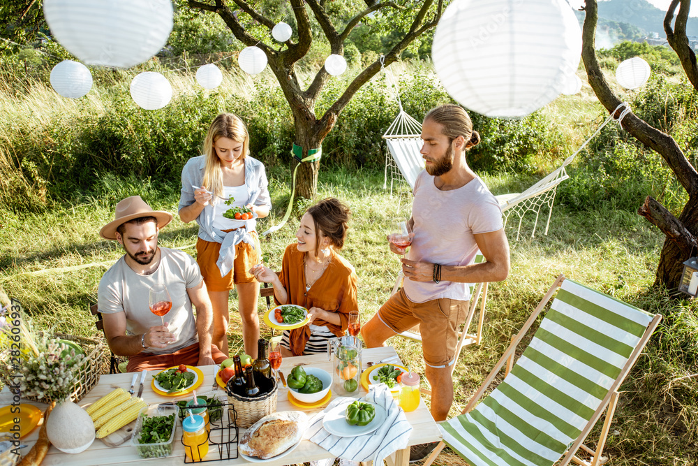 Group of a young friends having festive lunch in the beautifully decorated garden on a summer aftern