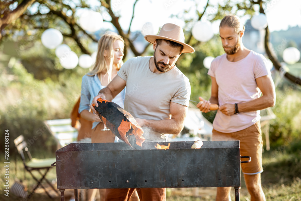 Group of a young friends having barbecue, cooking food in the beautiful garden during a festive lunc