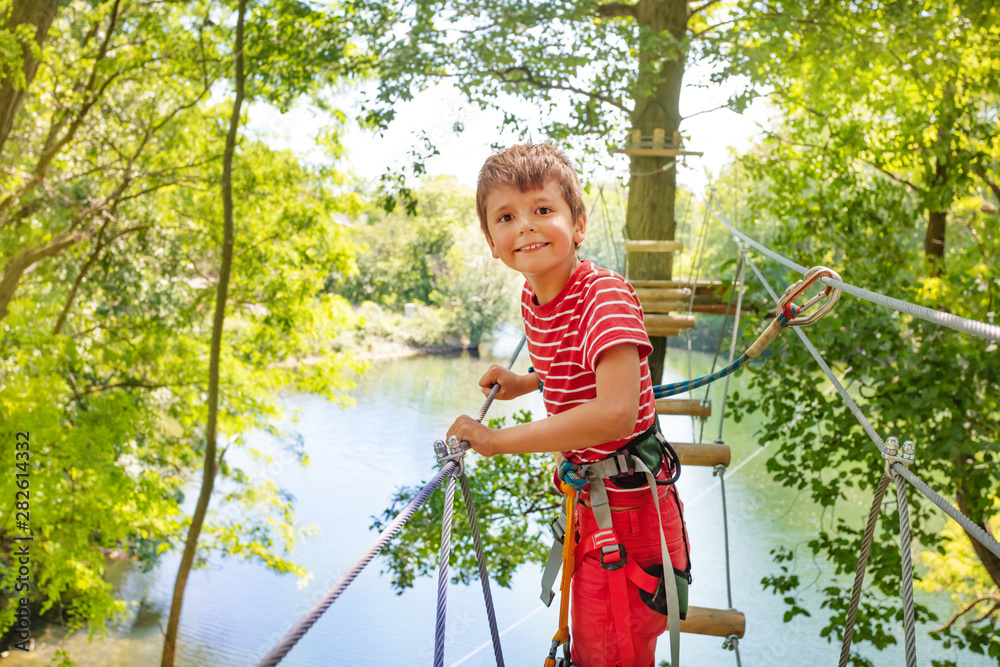 Happy boy on tree rope bridge in adventure park