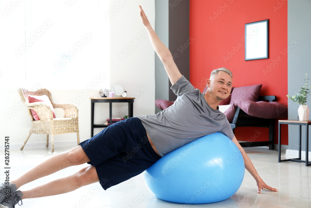 Young man doing exercise with fitball at home