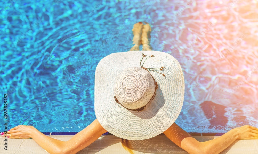 Beautiful woman in a hat sitting on the edge of the swimming pool