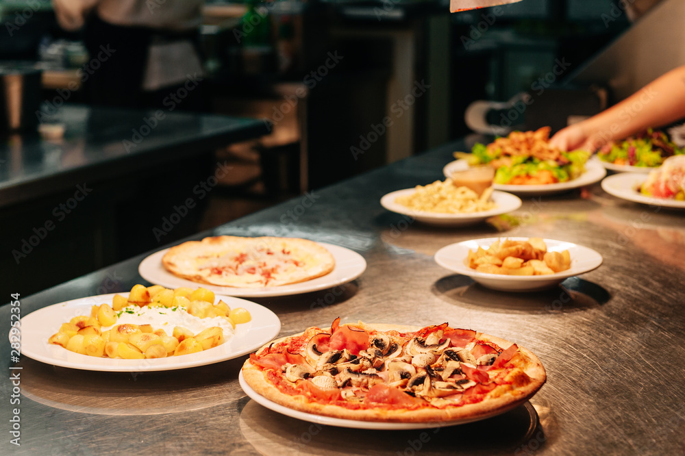 Food orders on the kitchen table in the restaurant, pizza with ham and mushrooms champignons, potato