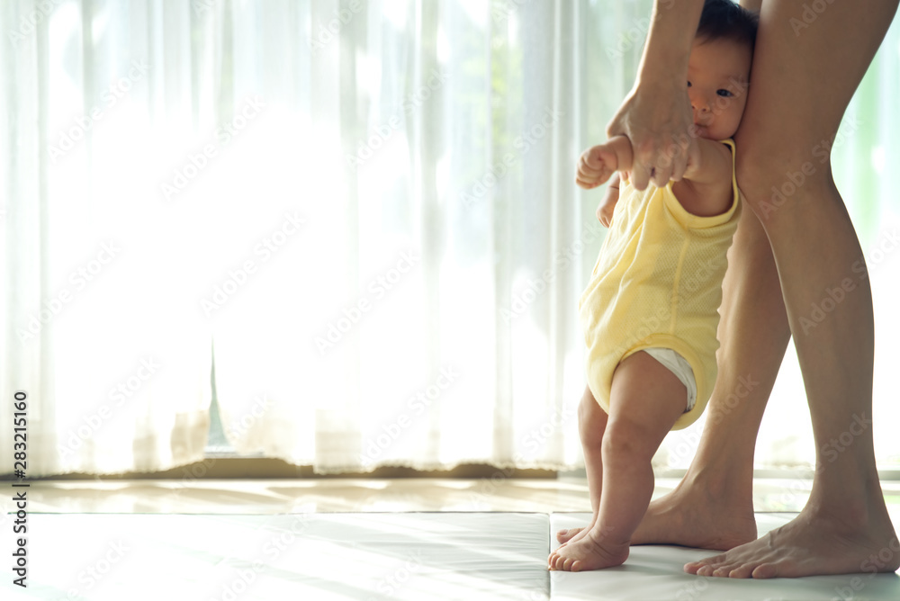 Asian baby taking first steps walk forward on the soft mat. Happy little baby learning to walk with 