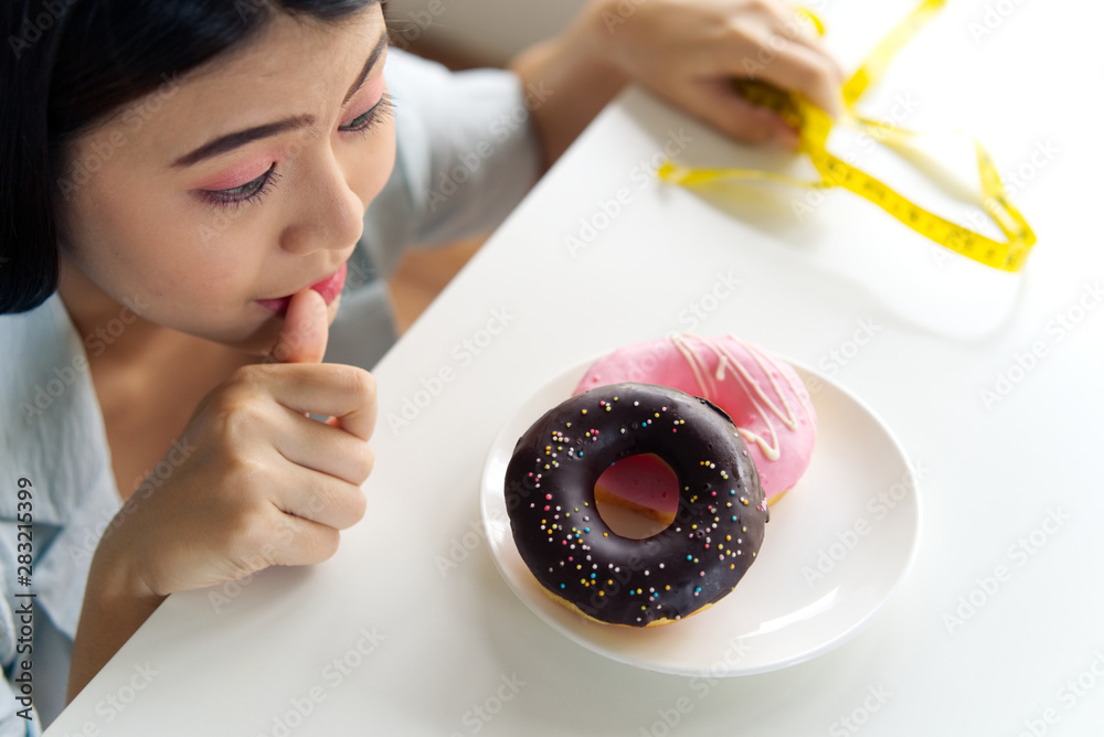 Close up portrait of Asian girl feeling greedy hungry licking finger wanting to eat donuts as junk o