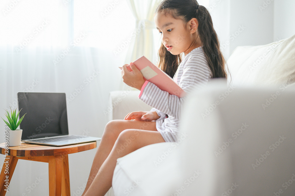 happy child little asian girl  reading a books on the table in the living room at home. family activ