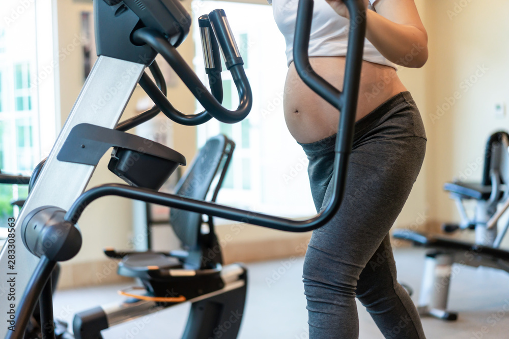 Active pregnant woman exercise in fitness center at yoga room. The young expecting mother holding ba