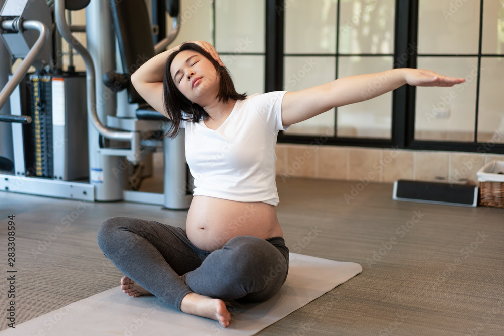 Active pregnant woman exercise in fitness center at yoga room. The young expecting mother holding ba