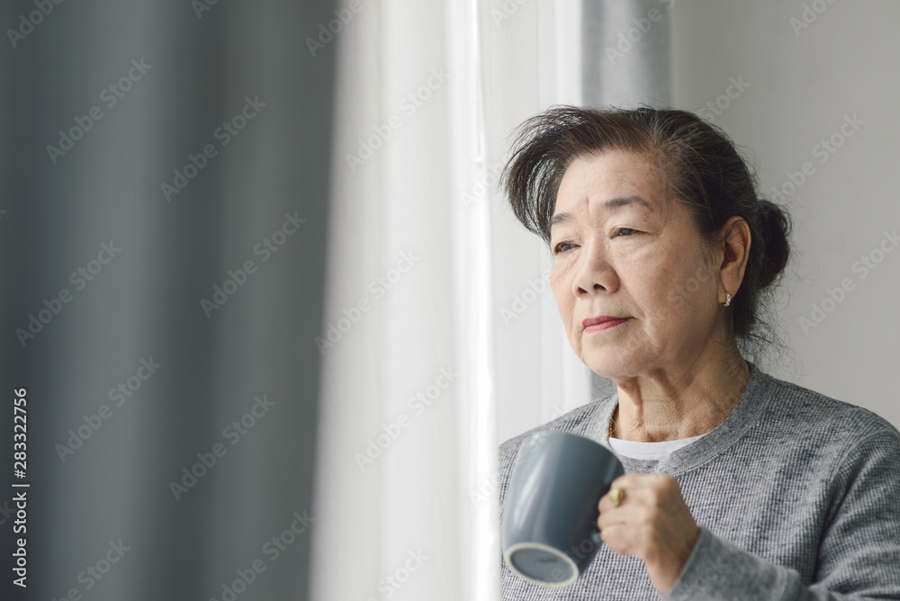 亚洲资深女性在户外靠窗喝热茶，孤独的概念。