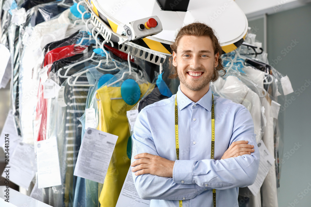 Worker of modern dry-cleaners near rack with clothes