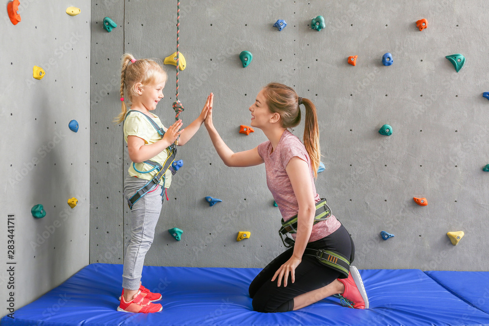 Little girl and instructor giving each other high-five in climbing gym