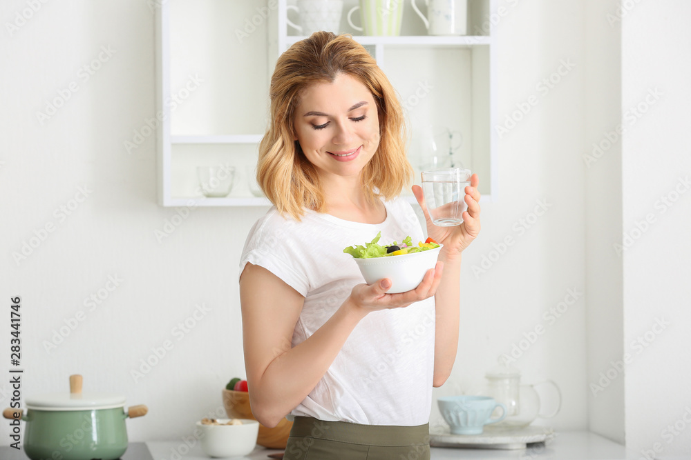 厨房里有健康蔬菜沙拉和一杯水的女人