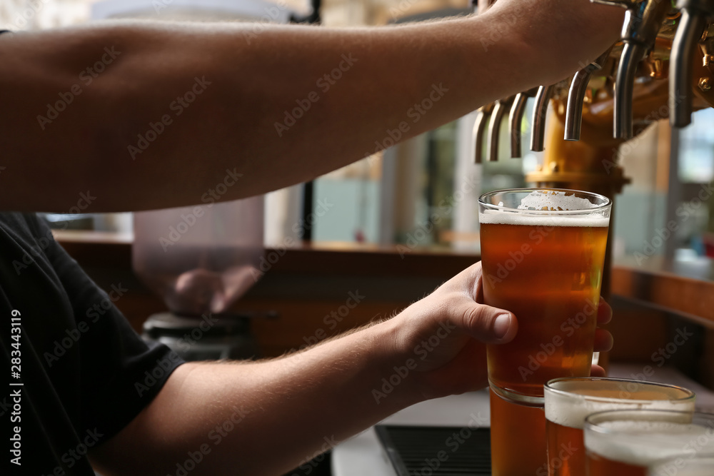 Barman pouring fresh beer in glass, closeup