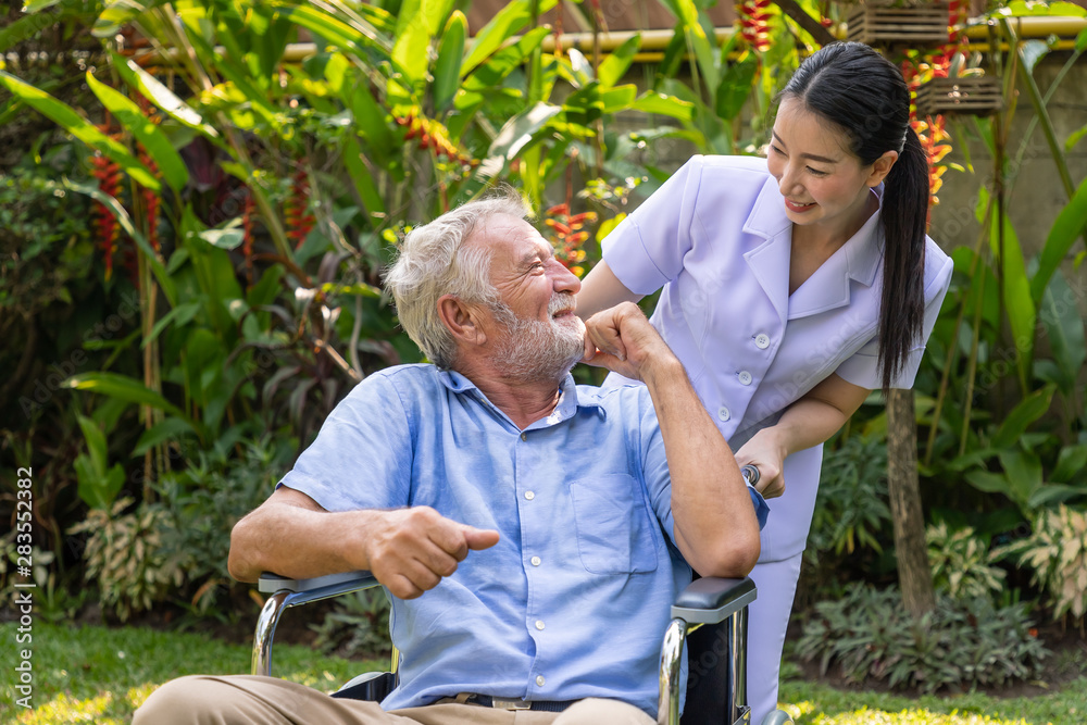 Happy nurse take care elderly man on wheelchair in garden at nursing home with thumb up