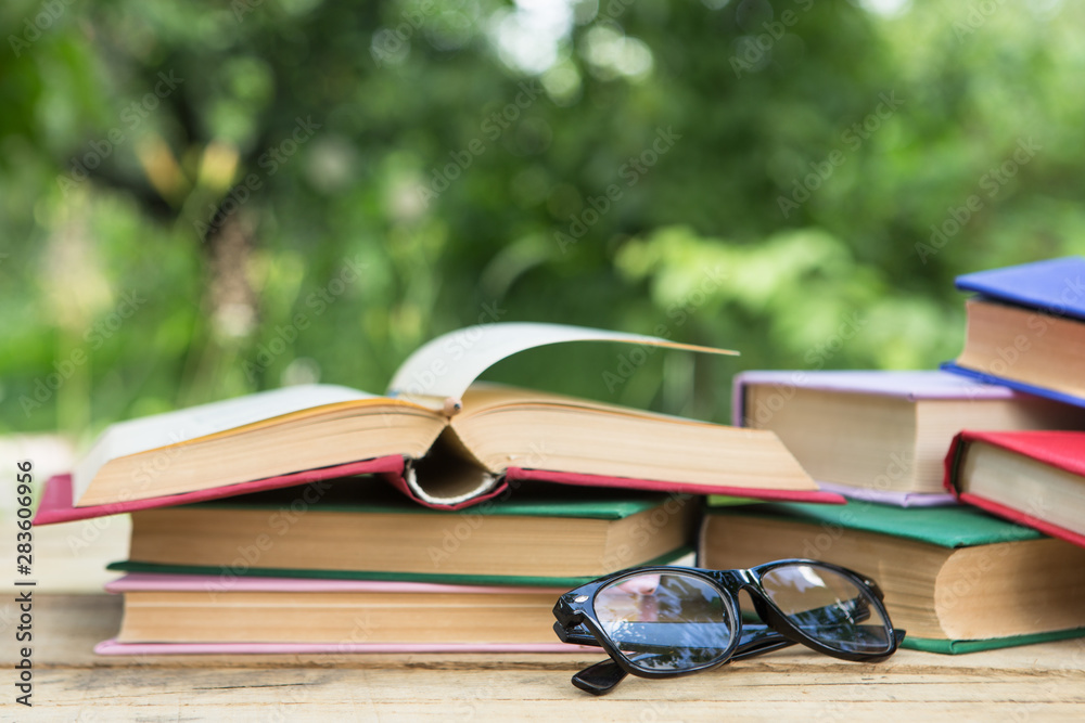 Open book and eyeglasses on a wooden table in a garden. Sunny summer day, reading in a vacation conc