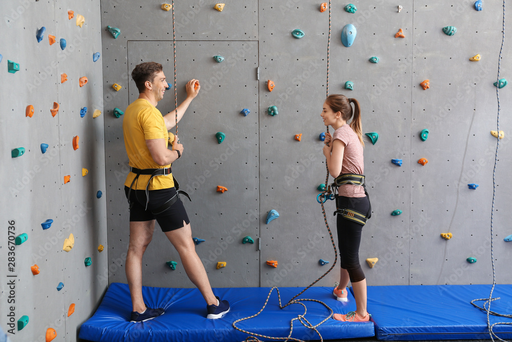 Young man with instructor climbing wall in gym