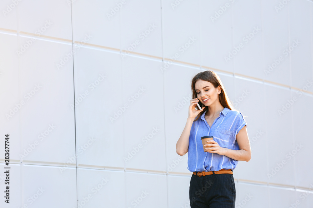 年轻的女商人拿着一杯美味的咖啡在户外用手机聊天