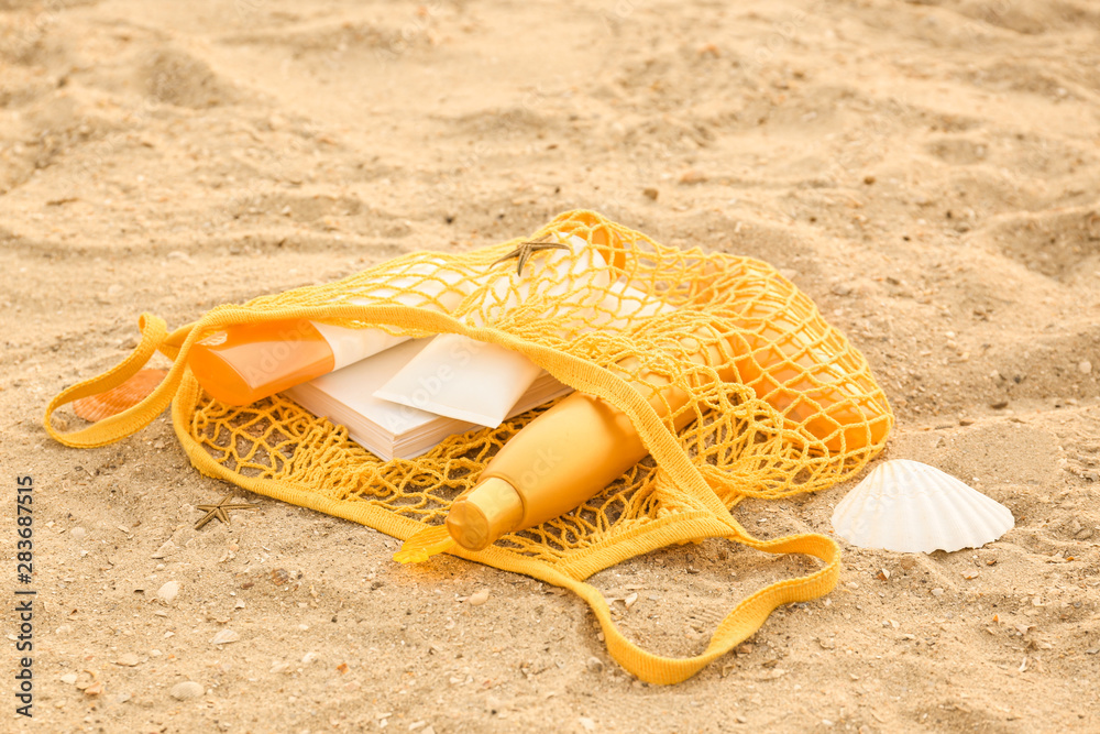 Bag with sunscreen cream and book on sand beach