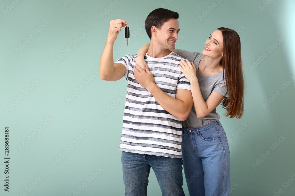 Happy couple with key from their new car on color background