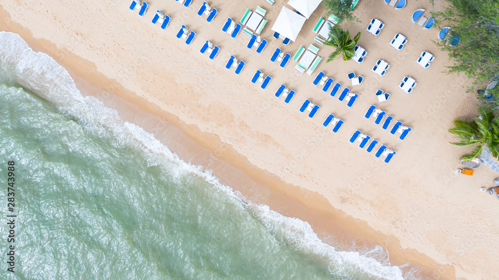 Aerial top view on the sandy beach. Umbrellas, sand, beach chairs and sea waves.