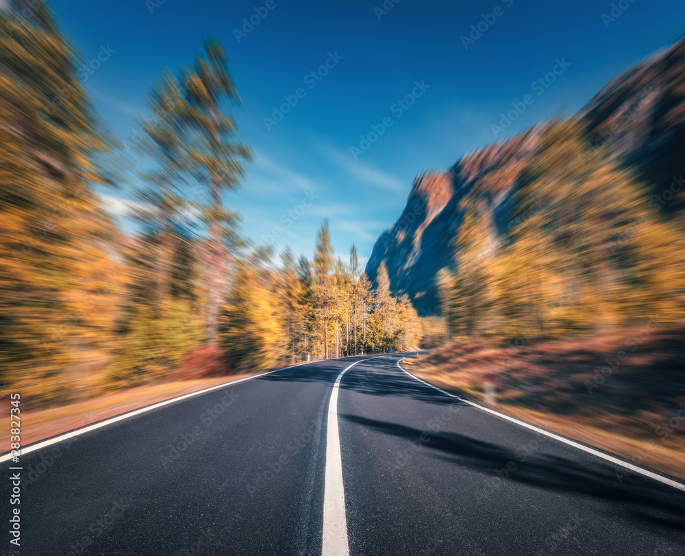 Mountain road in autumn forest at sunset with motion blur effect.  Asphalt road and blurred backgrou