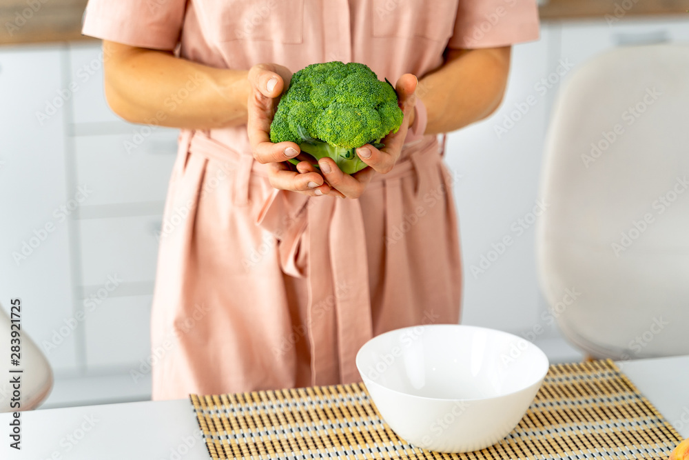 Young happy woman holding broccoli in the beautiful kitchen. Healthy food and Dieting concept. Loosi