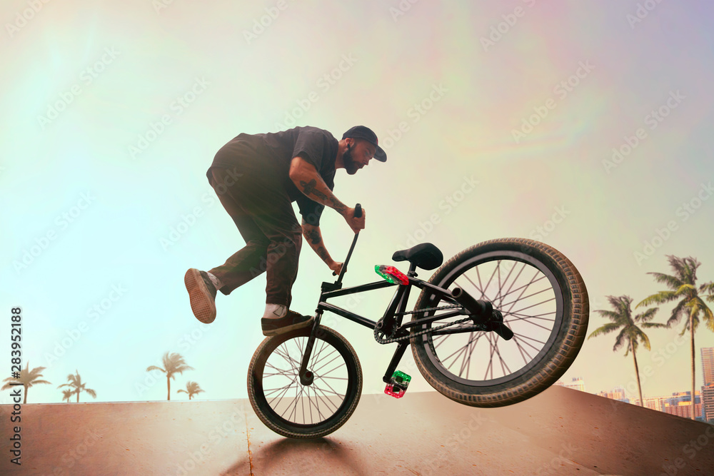 BMX rider is performing tricks in skatepark on sunset.