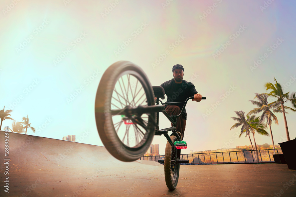 BMX rider is performing tricks in skatepark on sunset.