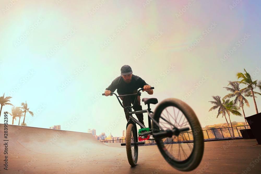 BMX rider is performing tricks in skatepark on sunset.