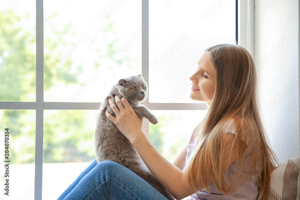 美丽的女人和可爱的猫坐在窗户附近