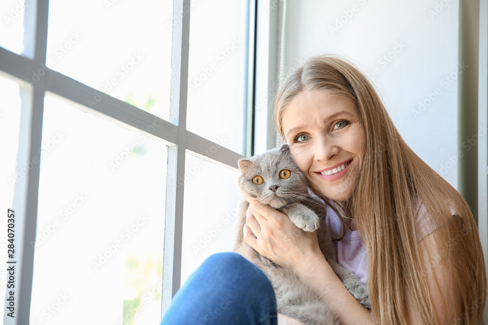 美丽的女人和可爱的猫坐在窗户附近