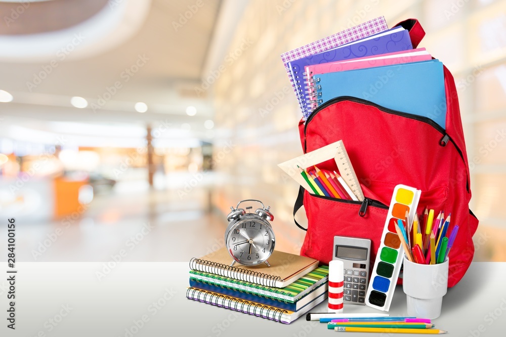 Colorful school supplies in backpack on blurred background