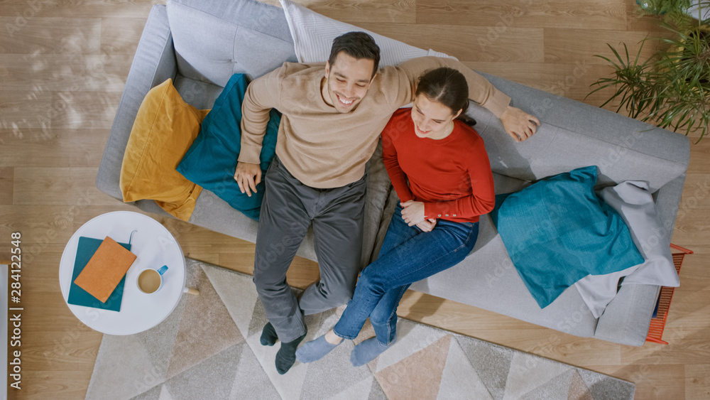 Young Beautiful Couple Sitting on a Couch with Pillows and Watching TV. They are Excited and Smile. 