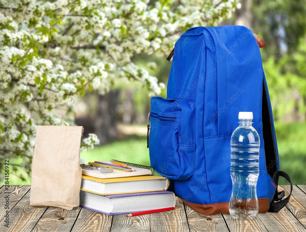 Colorful school supplies in backpack on wooden background