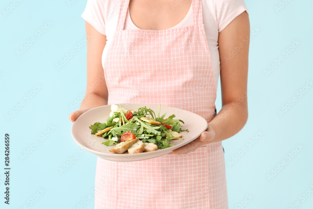 Woman holding plate with tasty arugula salad on color background, closeup