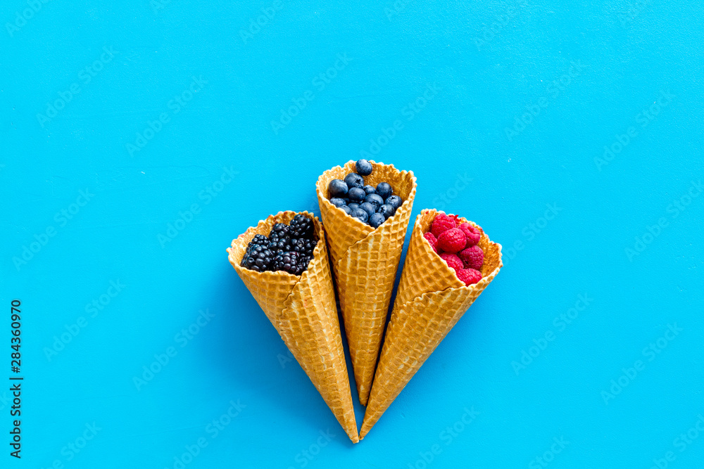 Summer breakfast with fresh berries in waffle cones on blue background top view mockup