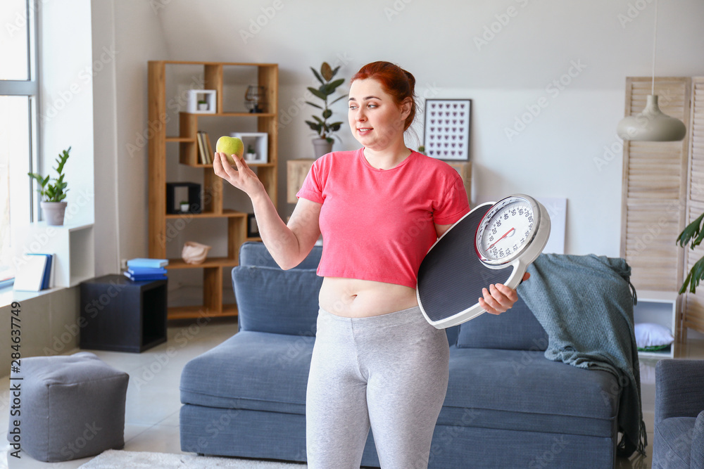 Overweight woman with apple and scales at home. Weight loss concept