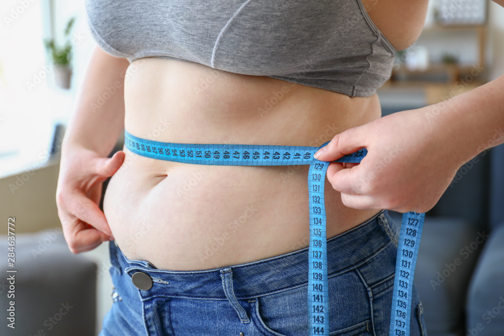 Overweight woman with measuring tape at home, closeup. Weight loss concept