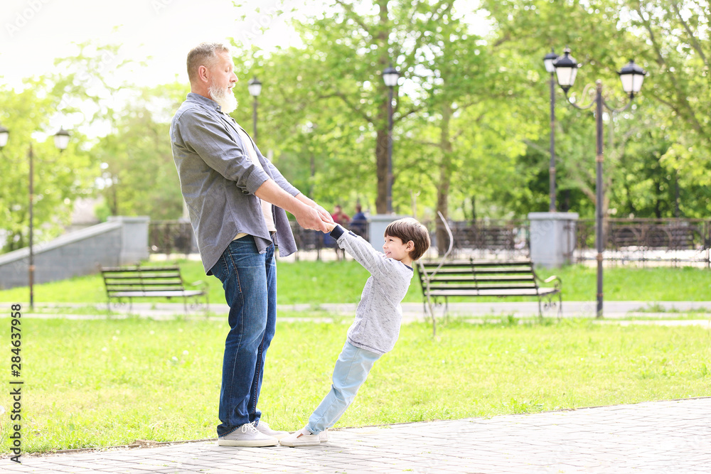 Cute little boy and his grandfather playing in park