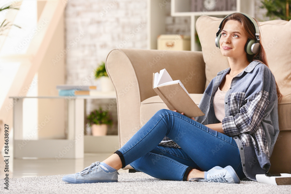 Beautiful young woman listening to music while reading book at home