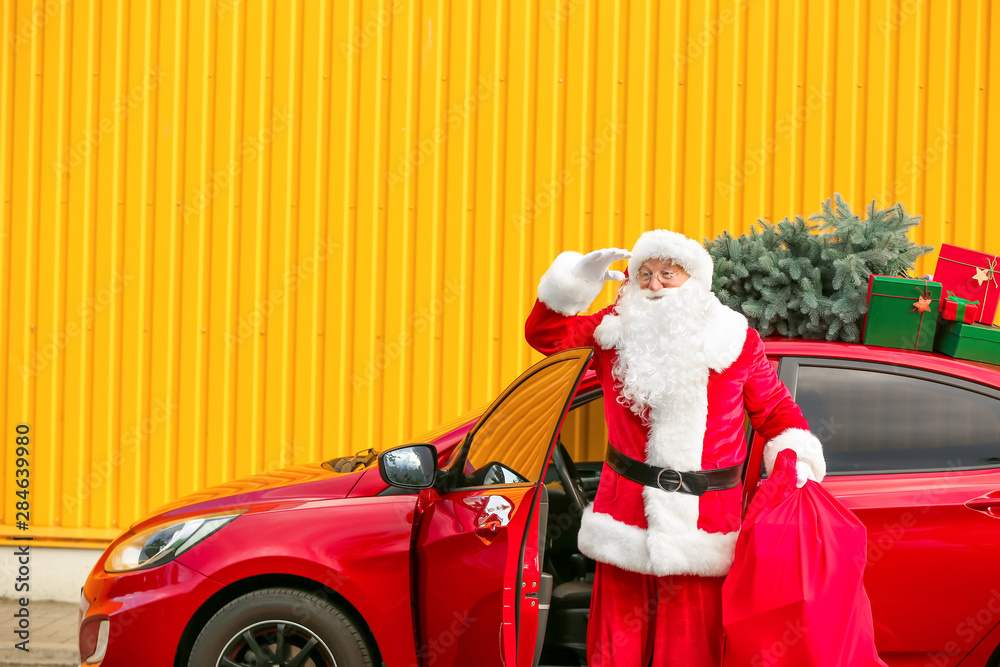 Santa Claus with gifts in bag looking far away near car outdoors