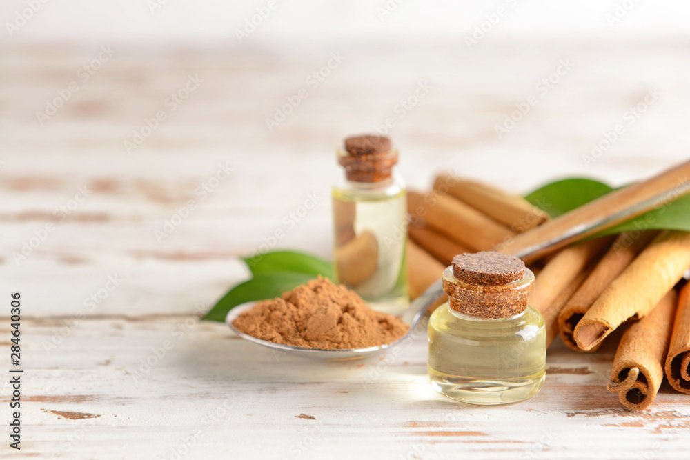 Aromatic cinnamon sticks, powder and essential oil on white wooden background