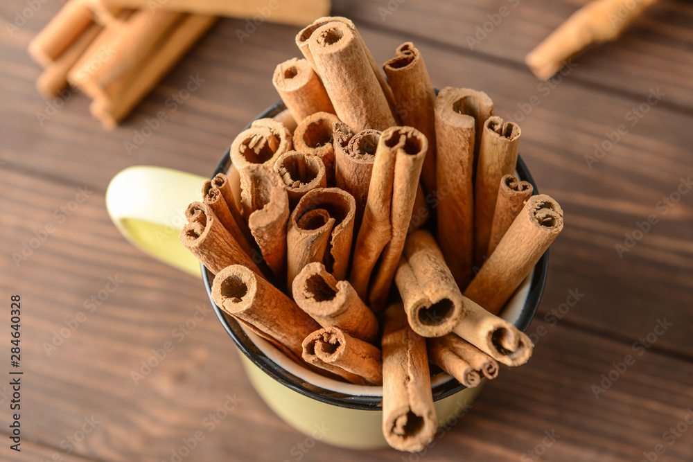 Mug with aromatic cinnamon sticks on wooden table